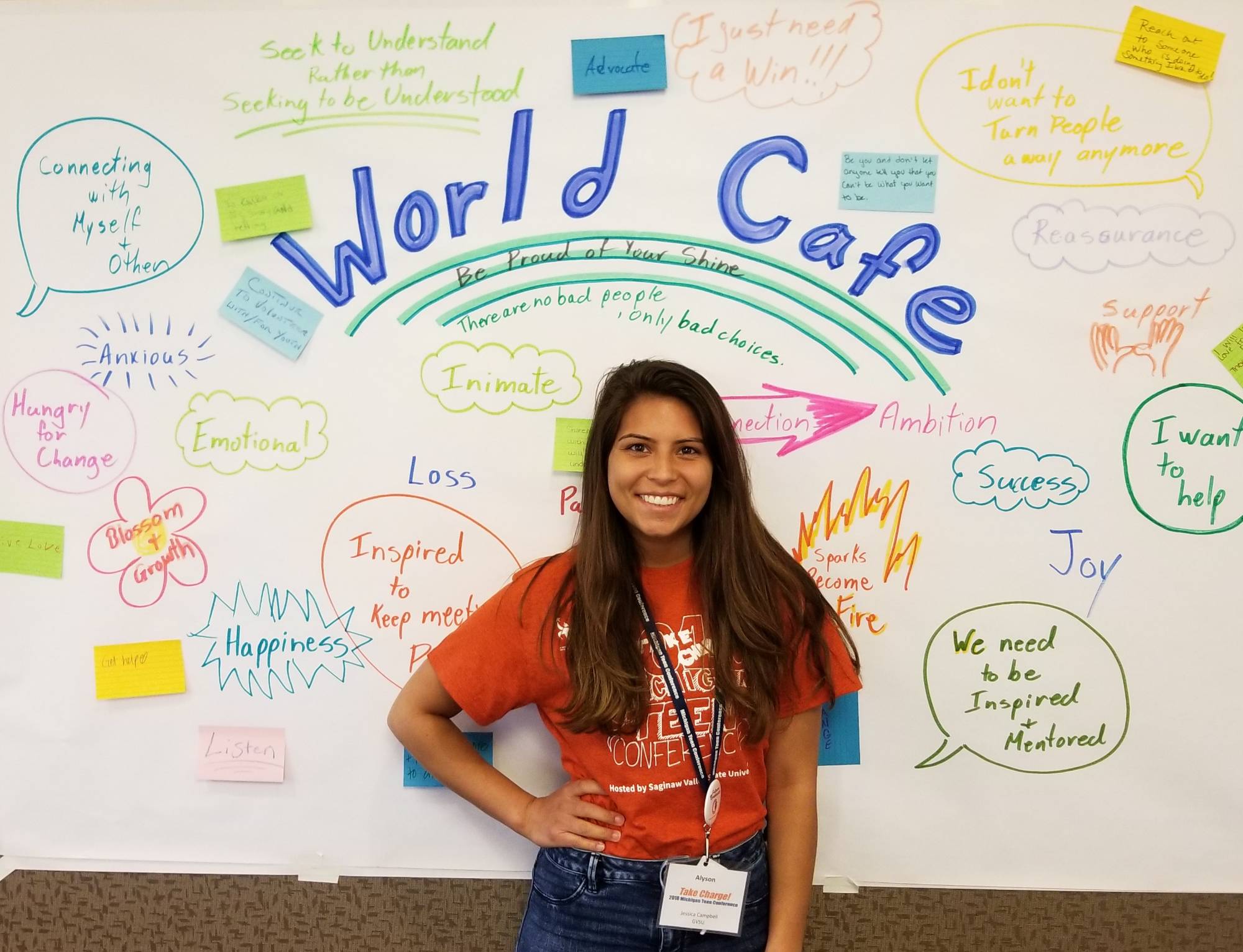 Smiling student standing in front of World Cafe poster